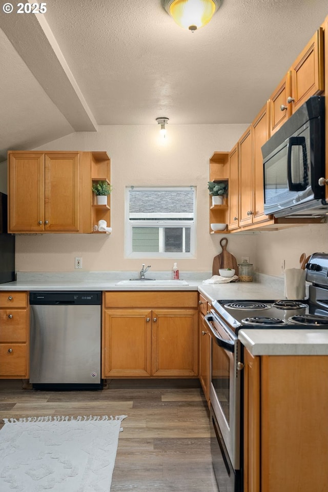 kitchen with sink, vaulted ceiling, a textured ceiling, appliances with stainless steel finishes, and light hardwood / wood-style floors