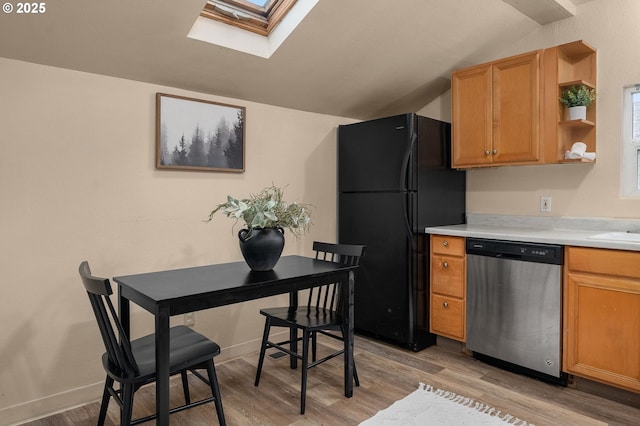 kitchen featuring lofted ceiling with skylight, stainless steel dishwasher, light hardwood / wood-style floors, and black fridge