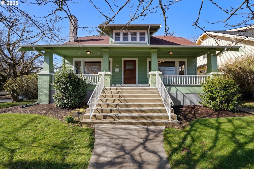 view of front facade with stairway, a chimney, a front lawn, and a porch