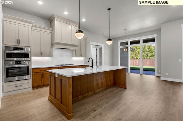 kitchen with appliances with stainless steel finishes, pendant lighting, tasteful backsplash, a large island, and light hardwood / wood-style flooring