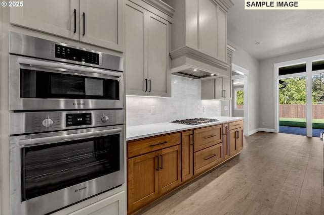 kitchen with premium range hood, tasteful backsplash, white cabinets, stainless steel appliances, and light hardwood / wood-style flooring