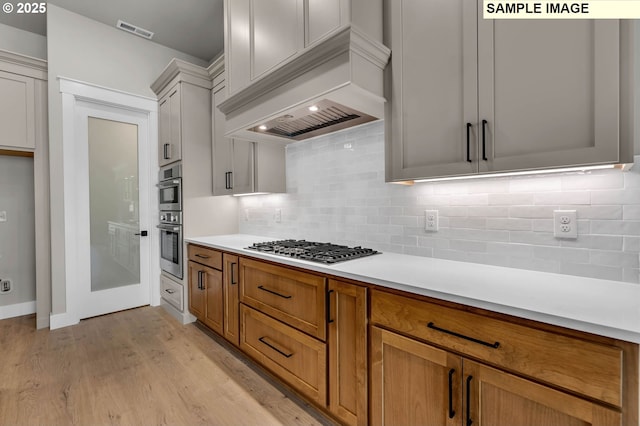 kitchen with premium range hood, stainless steel gas stovetop, white cabinets, backsplash, and light hardwood / wood-style flooring