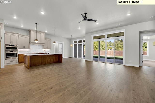 kitchen with tasteful backsplash, a large island with sink, ceiling fan, pendant lighting, and stainless steel double oven