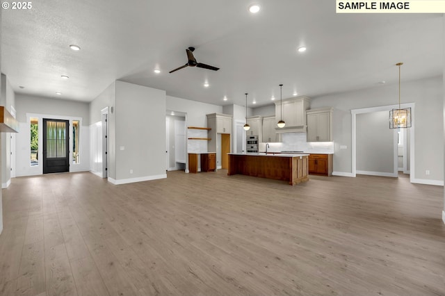 kitchen with ceiling fan with notable chandelier, decorative light fixtures, backsplash, a large island, and light hardwood / wood-style floors