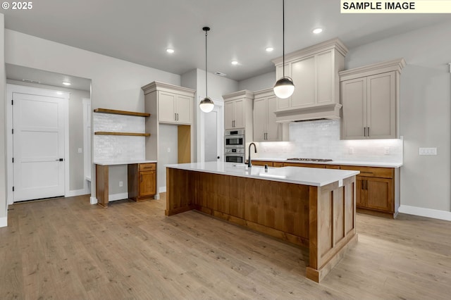 kitchen with hanging light fixtures, a center island with sink, decorative backsplash, custom exhaust hood, and light wood-type flooring