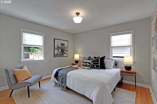 bedroom with multiple windows, wood finished floors, and baseboards
