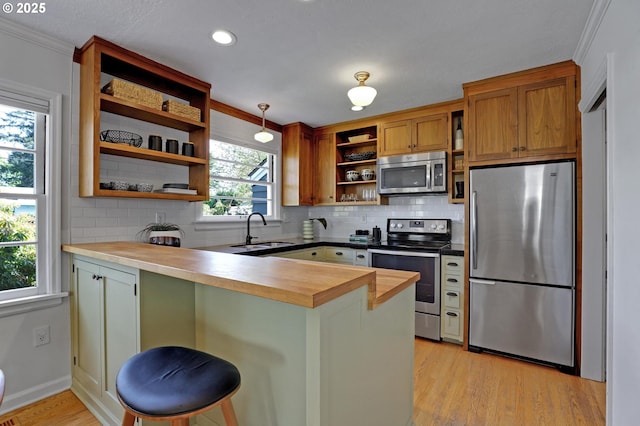 kitchen featuring stainless steel appliances, open shelves, wooden counters, a sink, and a peninsula