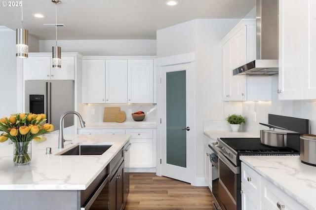 kitchen featuring appliances with stainless steel finishes, wall chimney exhaust hood, sink, decorative light fixtures, and white cabinetry