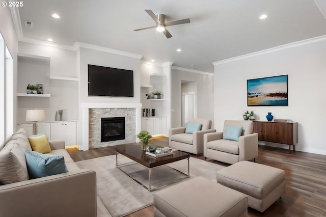 living room with a stone fireplace, ceiling fan, built in features, ornamental molding, and hardwood / wood-style flooring