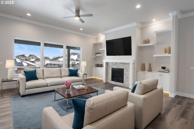 living room featuring a stone fireplace, built in shelves, ornamental molding, ceiling fan, and dark hardwood / wood-style floors