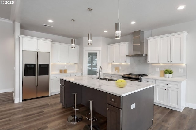 kitchen featuring white cabinetry, wall chimney range hood, sink, stainless steel appliances, and a center island with sink