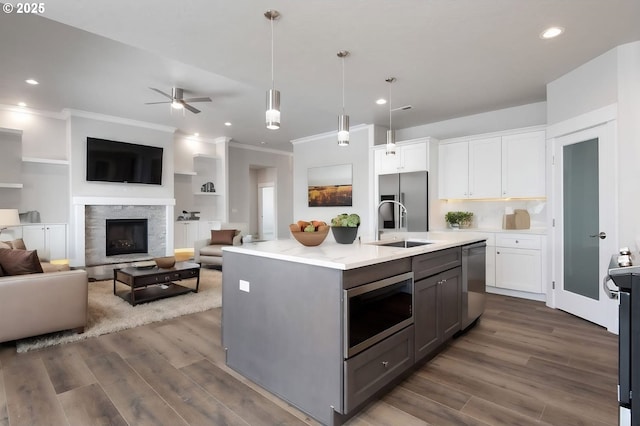 kitchen featuring white cabinets, stainless steel appliances, pendant lighting, and an island with sink