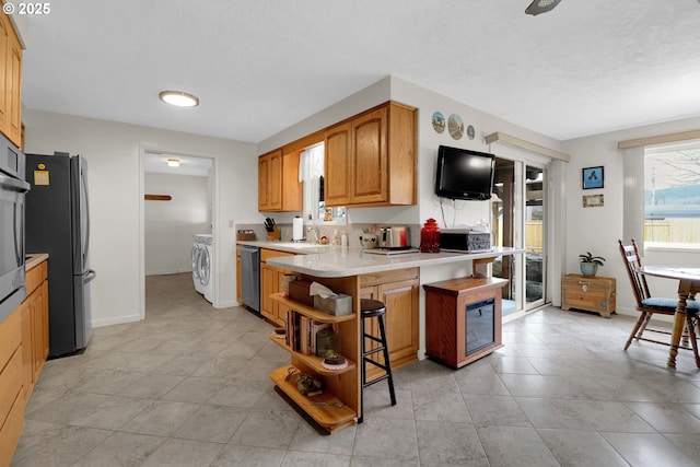 kitchen featuring washer and clothes dryer, a kitchen bar, light countertops, stainless steel appliances, and open shelves