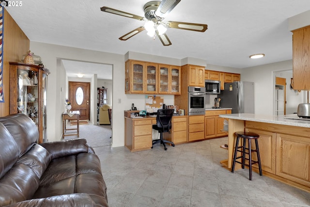 interior space featuring a breakfast bar, open floor plan, appliances with stainless steel finishes, glass insert cabinets, and ceiling fan