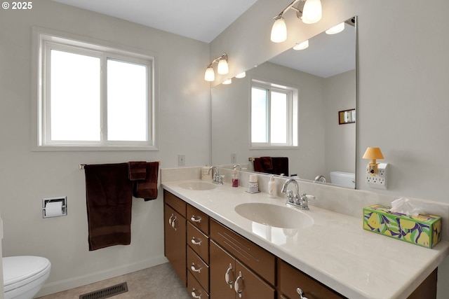 bathroom featuring double vanity, toilet, visible vents, and a sink