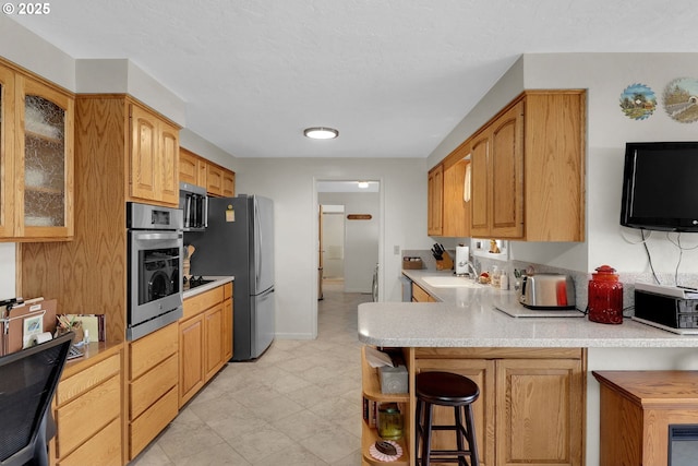 kitchen with a kitchen bar, appliances with stainless steel finishes, a peninsula, light countertops, and glass insert cabinets