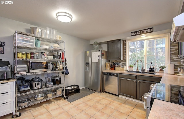 kitchen with range hood, sink, light tile patterned floors, stainless steel appliances, and dark brown cabinets