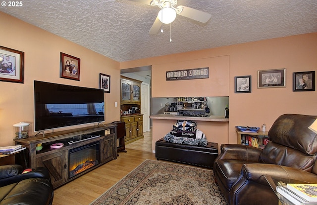 living room featuring ceiling fan, light hardwood / wood-style floors, and a textured ceiling