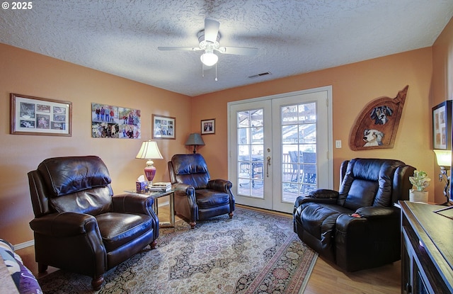 living area featuring ceiling fan, a textured ceiling, light hardwood / wood-style floors, and french doors