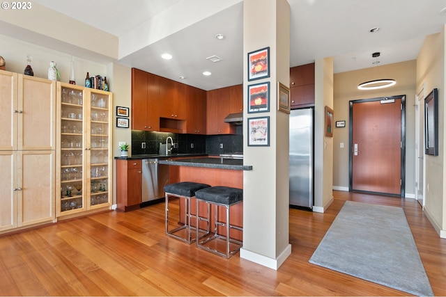 1025 NW Couch St Unit 613, Portland, OR 97209 - kitchen featuring a kitchen bar, dark countertops, a sink, stainless steel appliances, and light wood finished floors