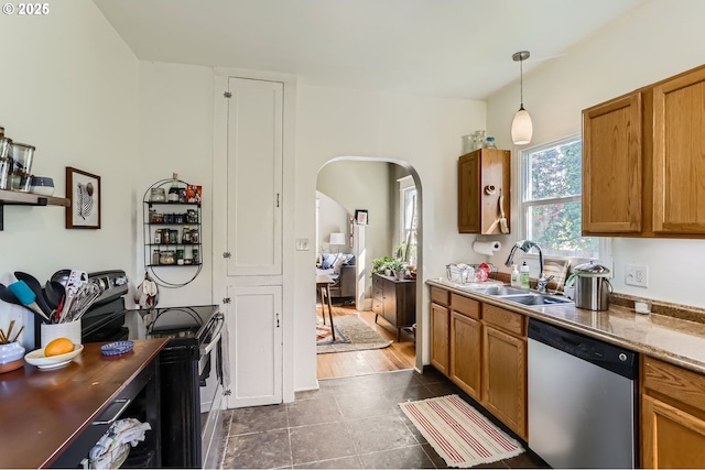 kitchen featuring a sink, arched walkways, appliances with stainless steel finishes, and brown cabinets