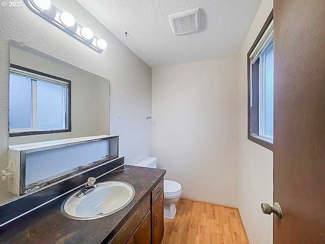 bathroom featuring a textured ceiling, toilet, wood finished floors, vanity, and visible vents