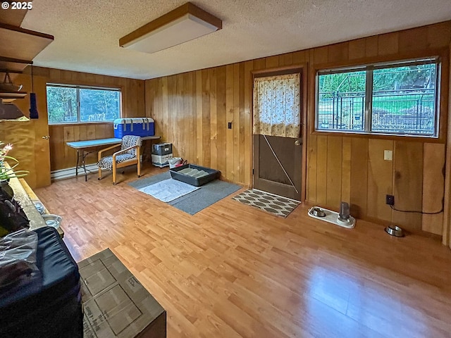 living area featuring a textured ceiling, a healthy amount of sunlight, wood finished floors, and wood walls