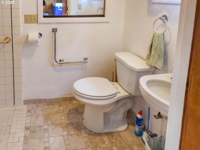 bathroom featuring stone tile floors, toilet, baseboards, and a sink