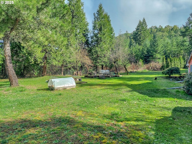 view of yard featuring an outdoor structure, a greenhouse, and a wooded view