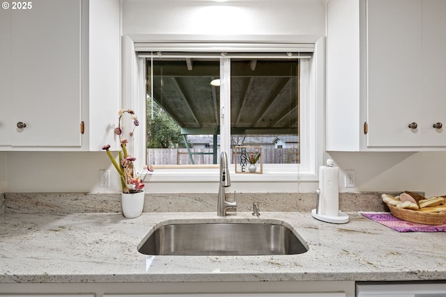 room details with sink, light stone countertops, and white cabinets