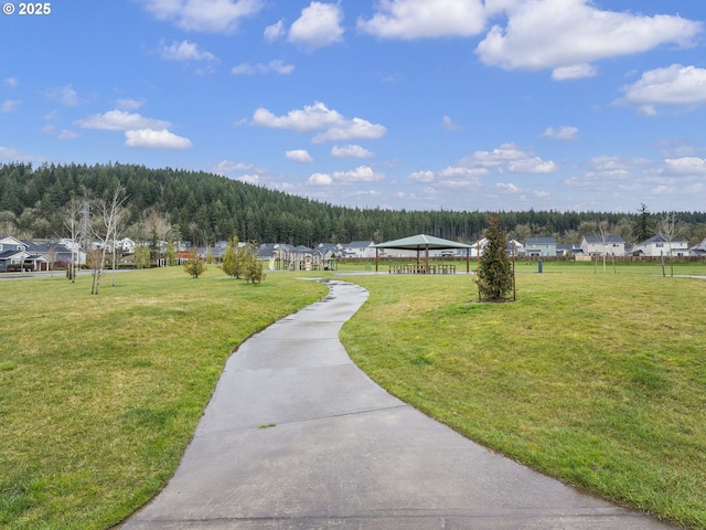 view of property's community with a gazebo, a forest view, and a lawn