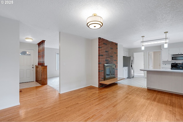 11184 S Allen Ct, Oregon City, OR 97045 - unfurnished living room featuring light wood-style floors, a textured ceiling, and a brick fireplace