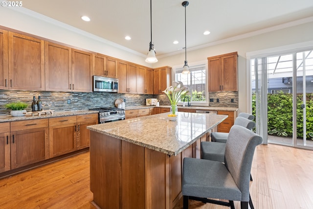 15152 NW Marie Way, Portland, OR 97229 - kitchen with appliances with stainless steel finishes, a breakfast bar area, a center island, brown cabinetry, and ornamental molding