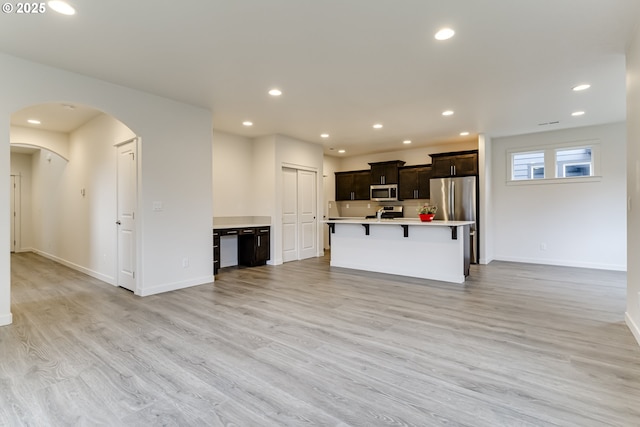 kitchen featuring a kitchen bar, light hardwood / wood-style floors, appliances with stainless steel finishes, tasteful backsplash, and an island with sink