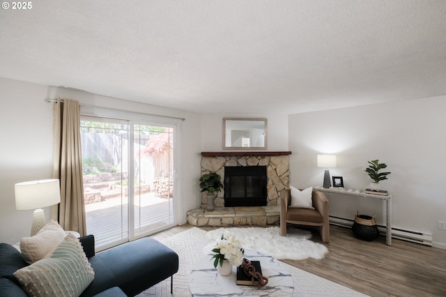 living area with a textured ceiling, a baseboard radiator, a stone fireplace, and wood finished floors