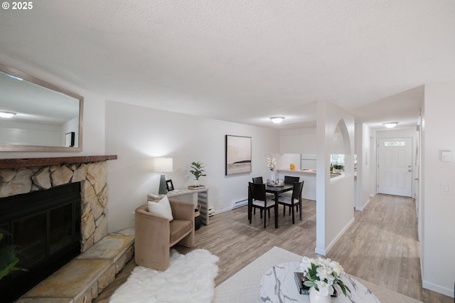 living room featuring baseboards, a textured ceiling, light wood-type flooring, and a stone fireplace