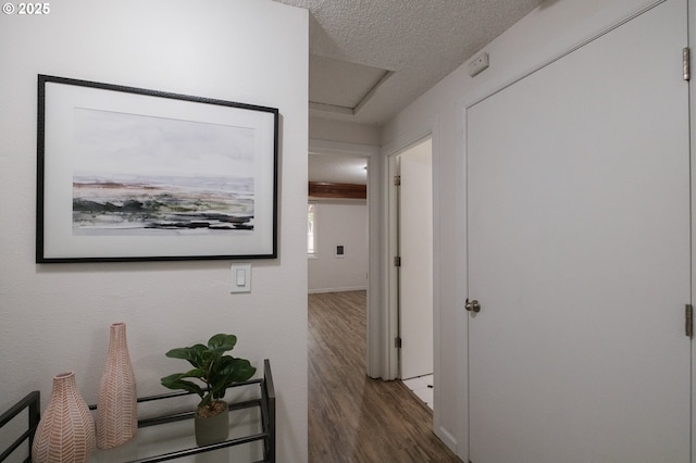 hallway with baseboards, attic access, a textured ceiling, and wood finished floors