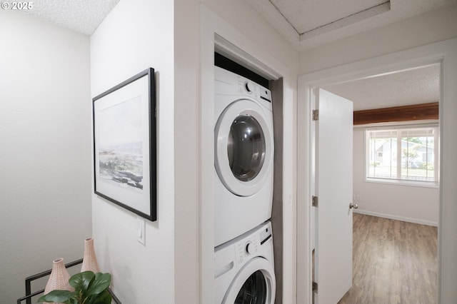 clothes washing area with laundry area, baseboards, stacked washing maching and dryer, a textured ceiling, and light wood finished floors
