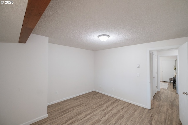 spare room featuring baseboards, light wood finished floors, and a textured ceiling