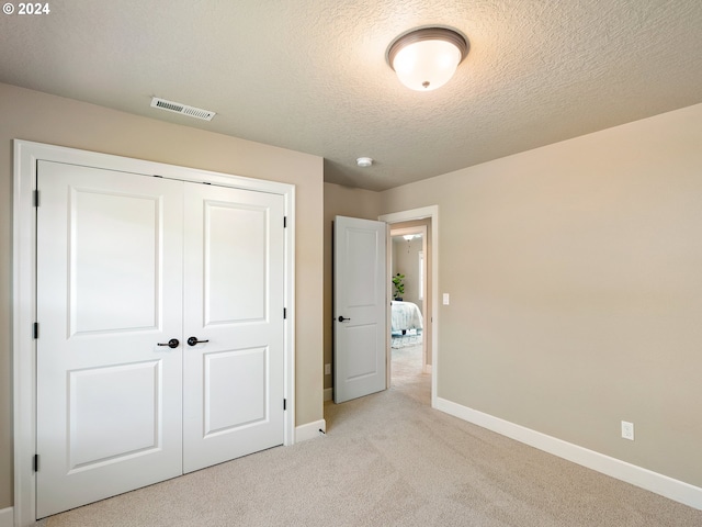 unfurnished bedroom with a textured ceiling, light carpet, visible vents, baseboards, and a closet