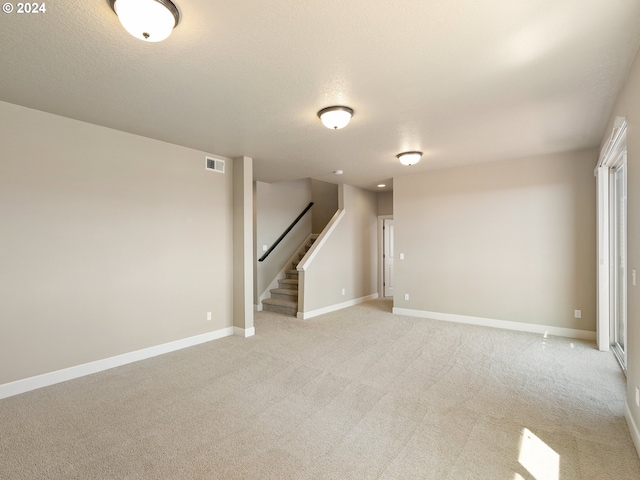 below grade area featuring light carpet, baseboards, visible vents, and stairway