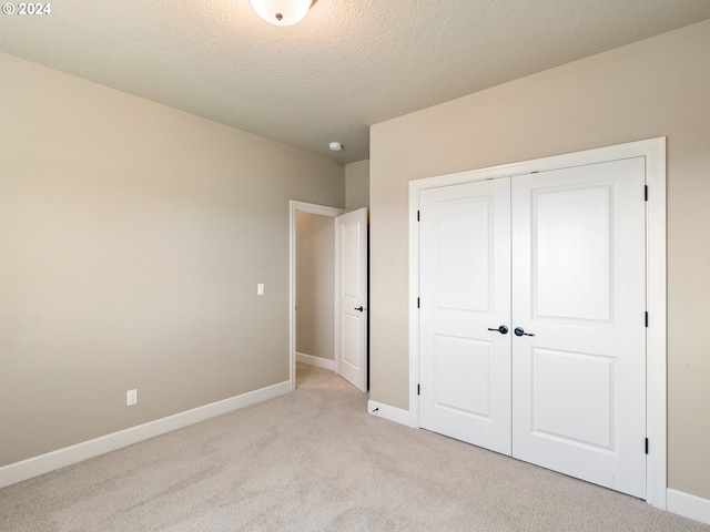 unfurnished bedroom featuring a closet, baseboards, a textured ceiling, and light colored carpet