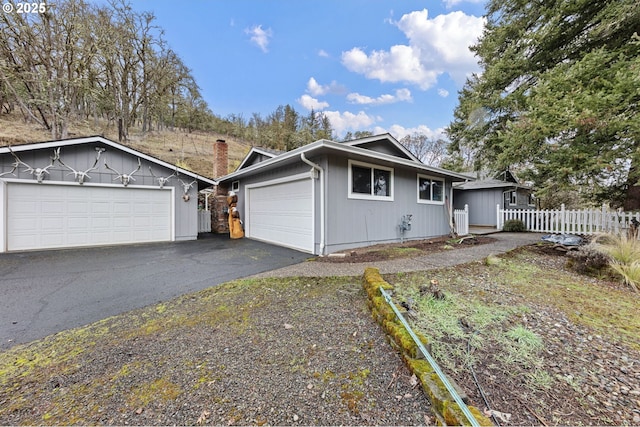 ranch-style house featuring driveway, a chimney, and fence