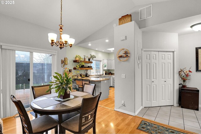 dining area with sink, vaulted ceiling, a chandelier, and light wood-type flooring