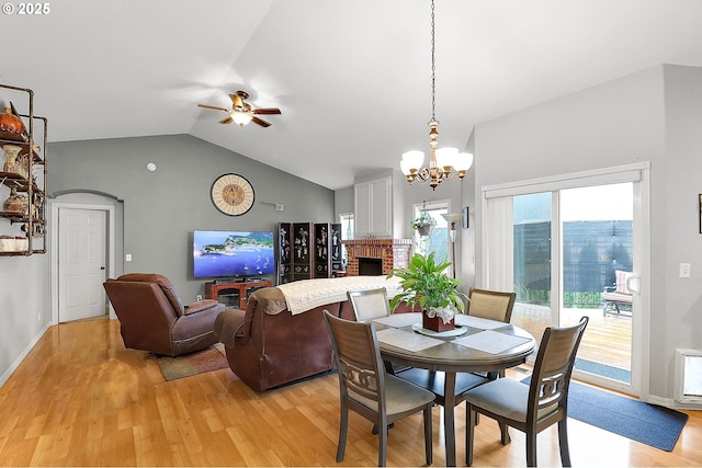 dining room with vaulted ceiling, light wood-type flooring, ceiling fan with notable chandelier, and a fireplace