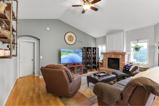 living room with baseboards, a ceiling fan, lofted ceiling, light wood-style flooring, and a brick fireplace