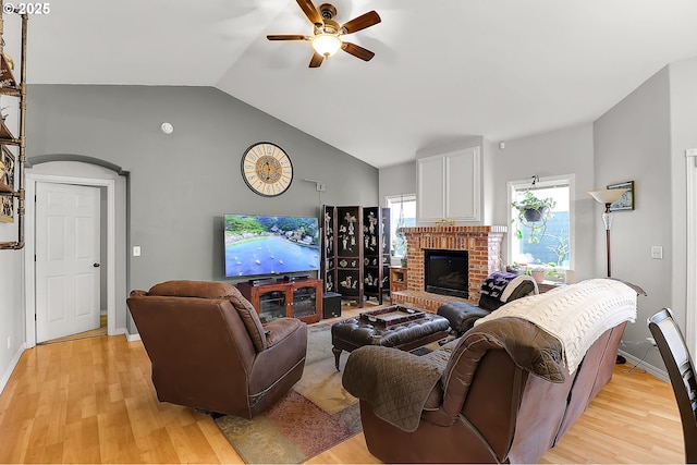 living area with baseboards, a ceiling fan, lofted ceiling, light wood-style flooring, and a fireplace