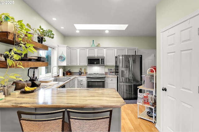 kitchen featuring a skylight, a peninsula, stainless steel appliances, light countertops, and a sink