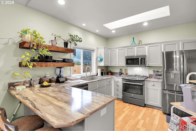 kitchen featuring a breakfast bar area, a peninsula, a skylight, a sink, and appliances with stainless steel finishes