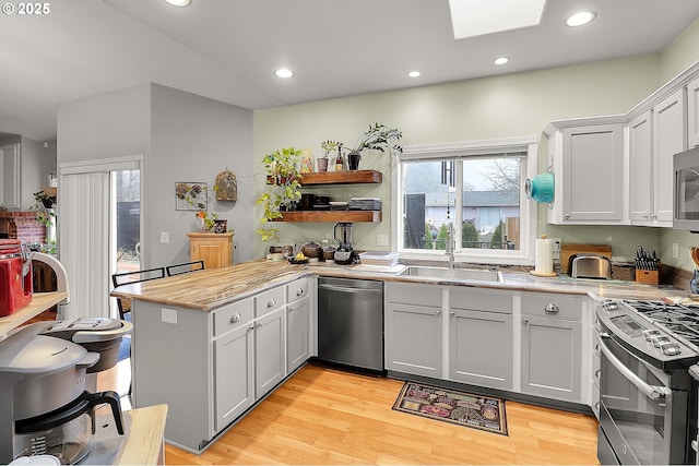 kitchen featuring a skylight, appliances with stainless steel finishes, light wood-style floors, a sink, and a peninsula